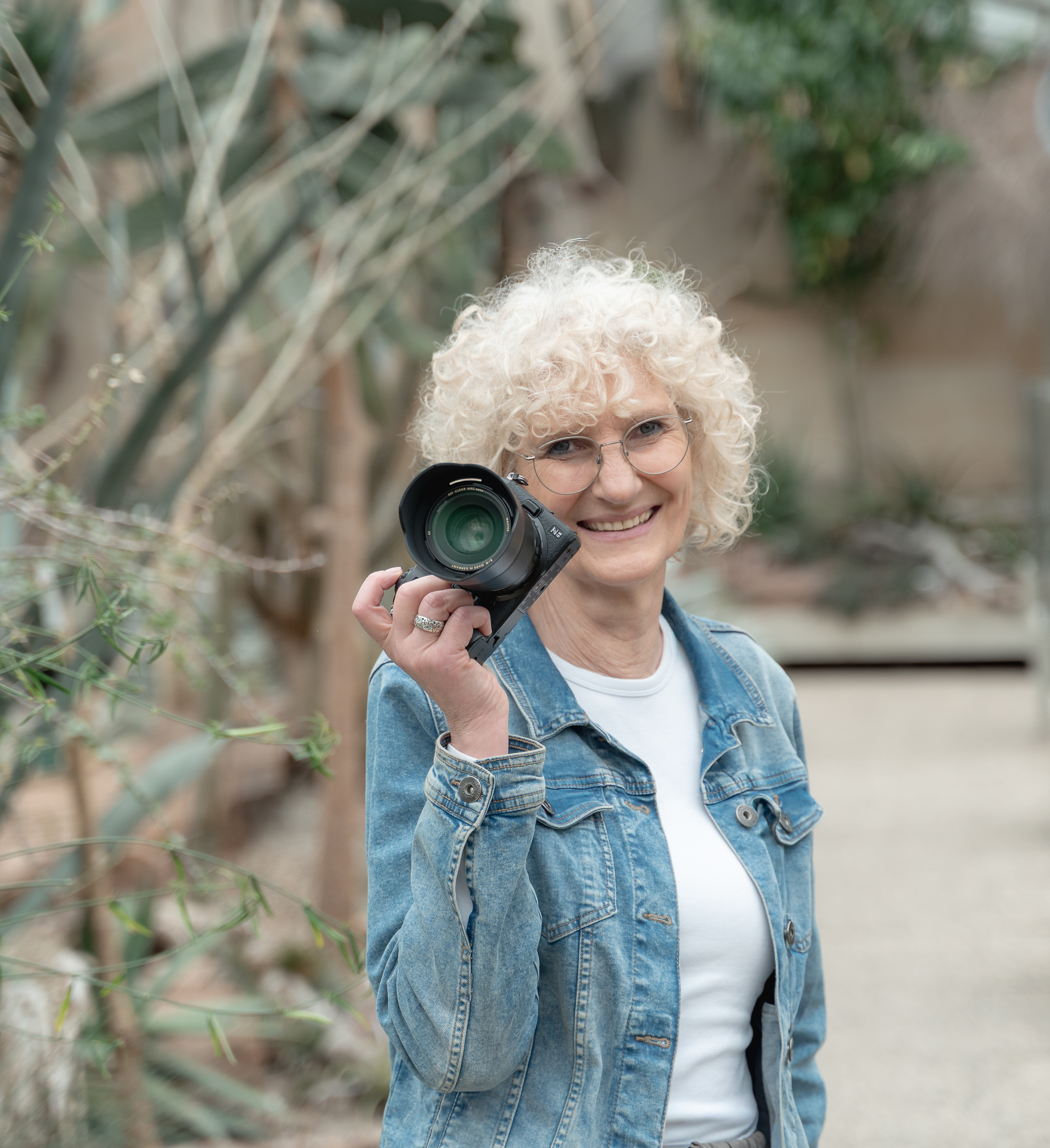 Fotografin lächelt in die Kamera und hält ihren Fotoapparat in Höhe des Gesichts.
