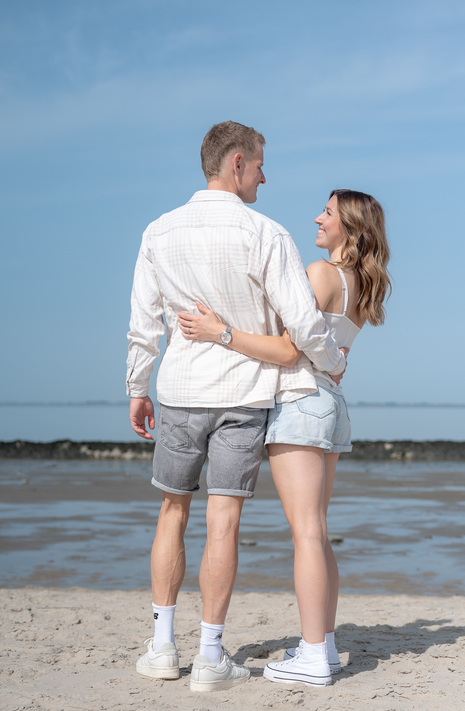 Ein Paar steht Arm in Arm am Strand und schaut sich in die Augen