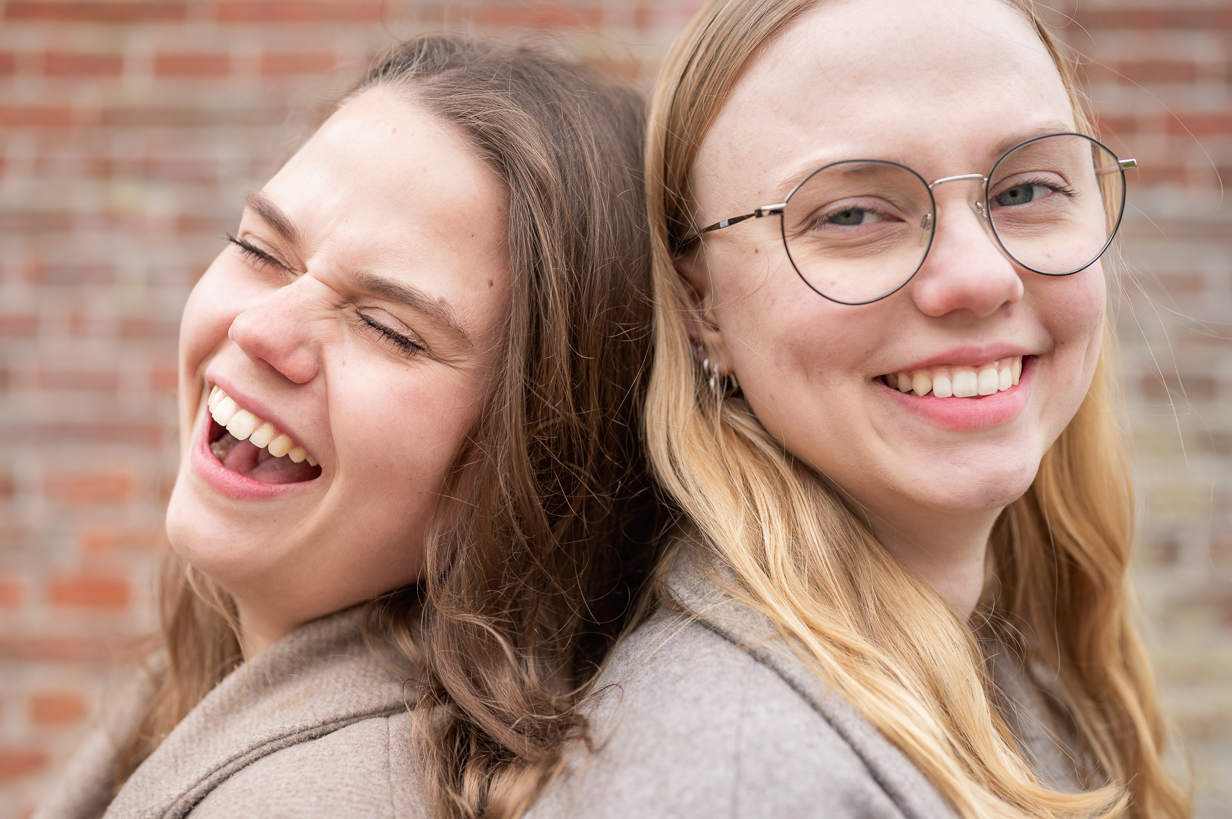 2 Schwestern stehen Rücken an Rücken und lachen sympathisch