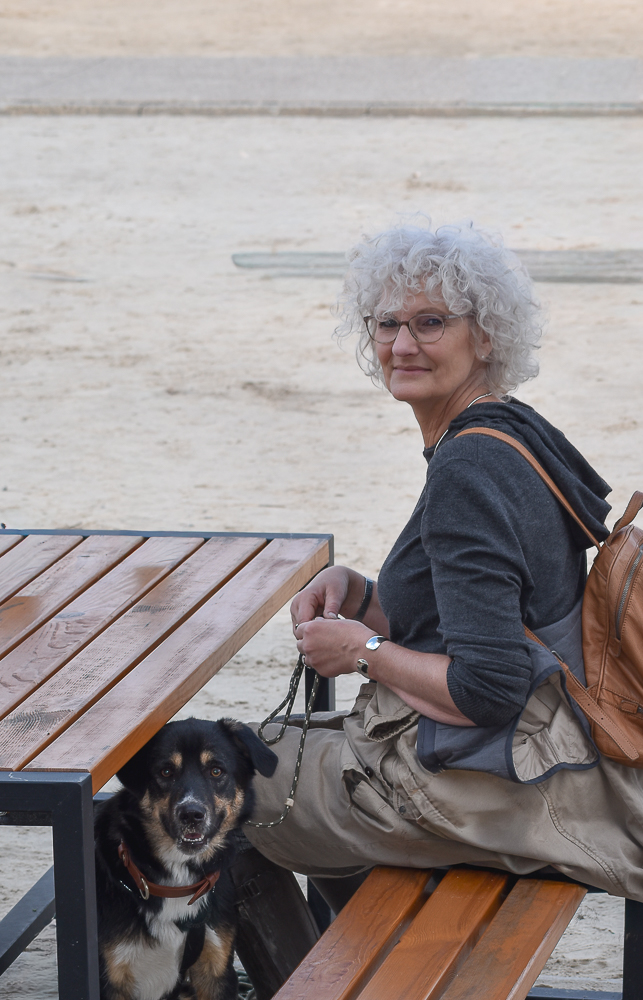 Frau lächelt verschmitzt in die Kamera am Strand.